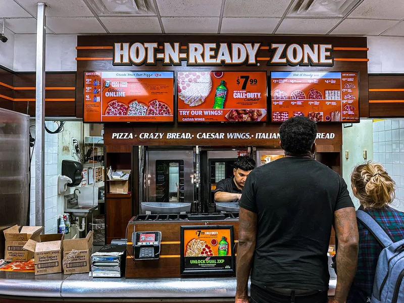 Bright digital menu boards above a busy pizza restaurant counter